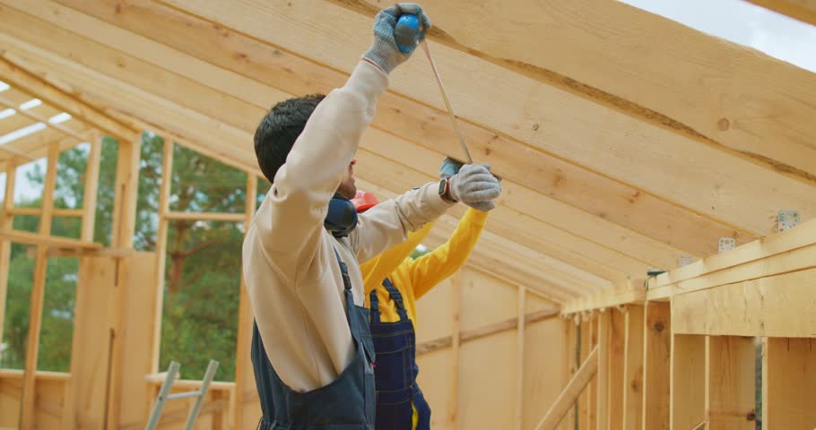 Team of man and woman builders in work uniform and hardhat using measuring tape. couple builds house out of wood. Builders measure board with tape measure. Frame of wooden house near carpenter. | Shutterstock HD Video #1106225629