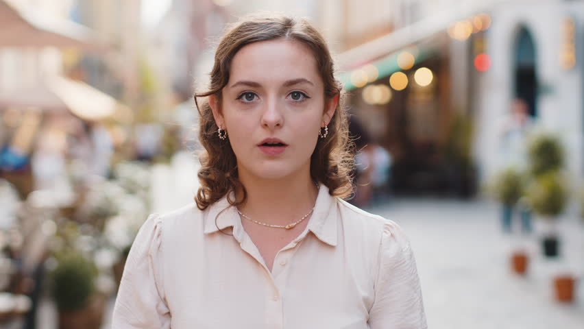 Oh my God, Wow. Young pretty woman looking surprised at camera with big open eyes, shocked by sudden victory, game winning, lottery goal achievement, good news outdoors. Lovely girl in city street Royalty-Free Stock Footage #1106232311