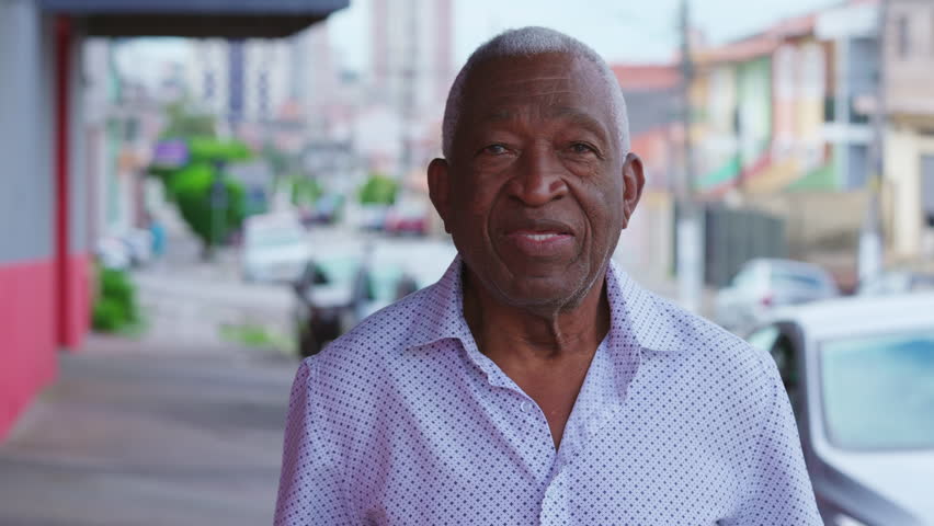 Portrait of a happy black senior Brazilian man standing in street sidewalk looking at camera with smiling expression. Elderly African American male with joyful emotion in urban setting Royalty-Free Stock Footage #1106232467