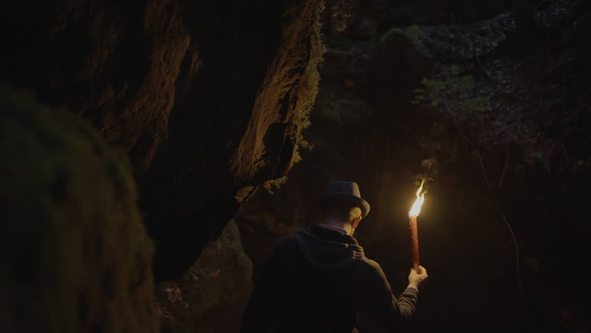 Young Man Discovering Stone Cave Outdoors at Night Holding Torchlight Royalty-Free Stock Footage #1106236119