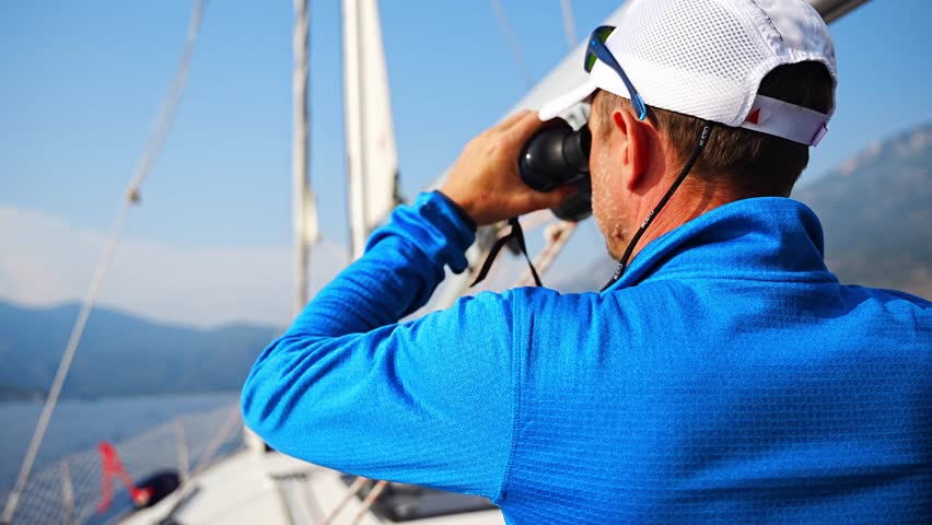 Young man captain on the yacht looking through binoculars during sailing boat control. Travel and active life. High quality 4k footage Royalty-Free Stock Footage #1106244799