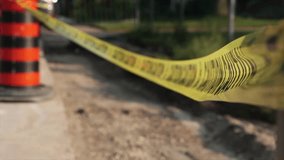 yellow and black caution tape blowing in wind tied to orange and black traffic delineator pylon barrel drum on street next to torn out pavement for watermain line replacement with blurred background - Powered by Shutterstock - Get 15% off with code: PIKWIZARD15