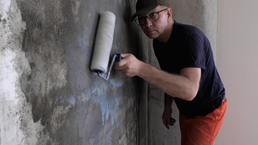 Un pintor pinta un muro de hormigón con pintura blanca, un macho de mano  con un rodillo de pintura para pintar una pared Fotografía de stock - Alamy