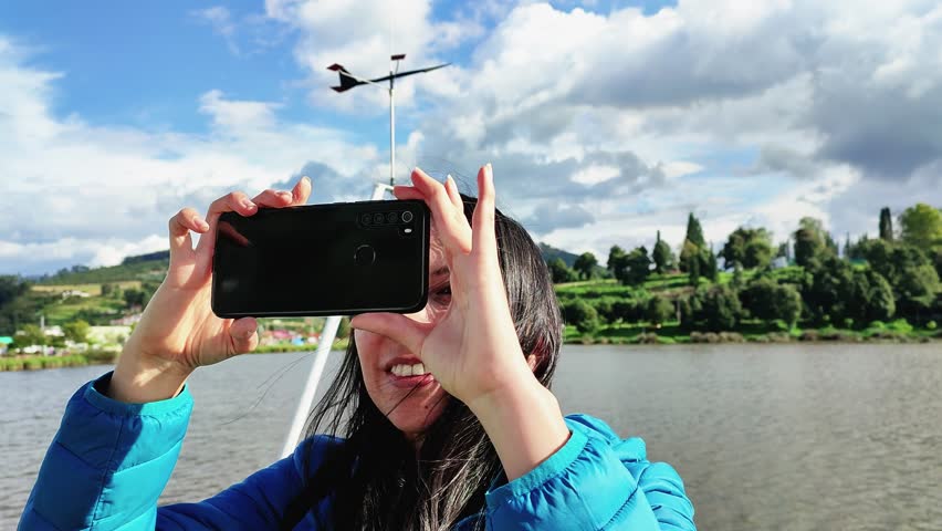 young woman taking pictures with her cell phone near a lake