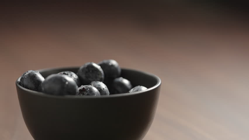 Slow motion fresh washed blueberries picked by man hand from black bowl