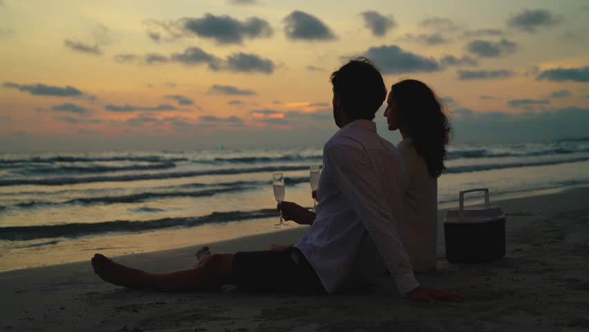 Standing side by side, a young couple gazes out at the sea with a deep sense of romance, their eyes fixed on the stunning sunset that paints the sky with a warm, orange glow. Slow motion shot. Royalty-Free Stock Footage #1106254725