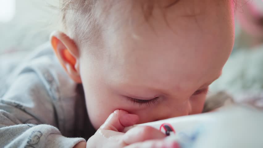 Baby laying on stomach, looking around, gnawing a package. An infant learning the world. Royalty-Free Stock Footage #1106257891