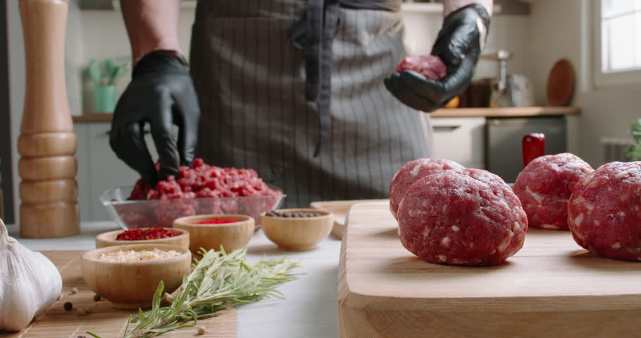 The cook prepares meatballs from minced meat using special forms on a wooden table with vegetables and spices Advertising. Fresh meat twisted into minced meat for making burger. Cook food Royalty-Free Stock Footage #1106258325