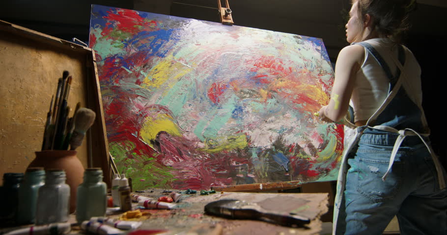 Millennial girl artist paints picture in loft studio puts paint on canvas with her hands. Abstract cinematic. Serious female artist is working at picture, painting technique and painters concept. Royalty-Free Stock Footage #1106258337