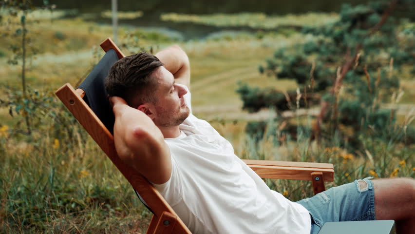 Caucasian man enjoying rest in the nature. Man sits comfortably in a folding chair, looking around.