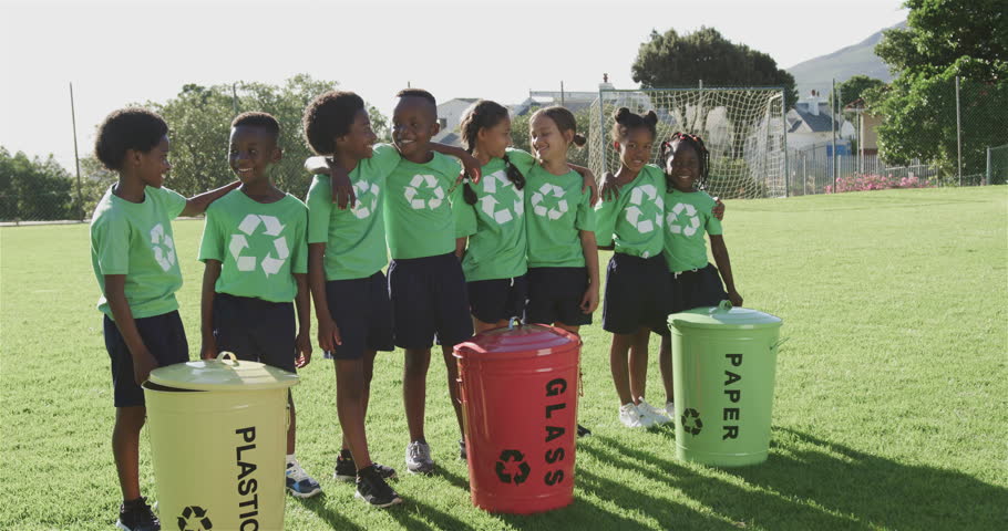 Portrait of happy diverse schoolchildren with recycling bins in sports field at elementary school. School, ecology and education, unaltered.