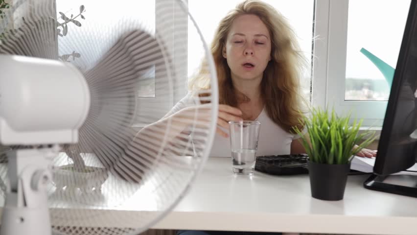 heat in the office,Woman blowing a fan to stay cool and comfortable, trying to cool down in a non-air-conditioned, office worker drinking water, Dehydration, heatstroke, summer heat Royalty-Free Stock Footage #1106261223