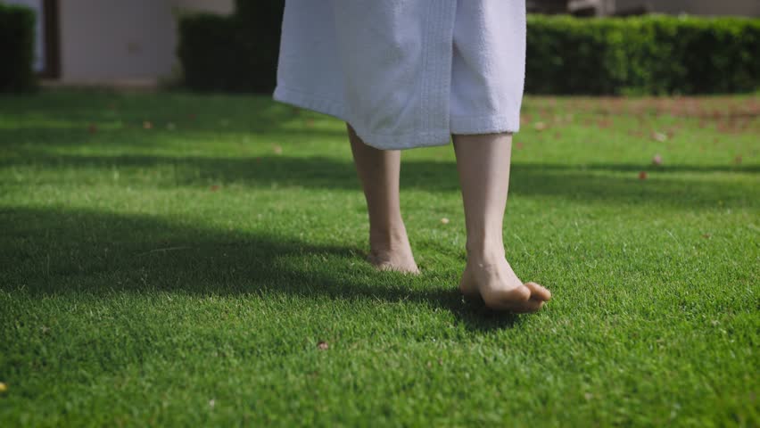 A woman in a white coat walks barefoot on a perfect lawn. Unity with nature and harmony. Royalty-Free Stock Footage #1106263057
