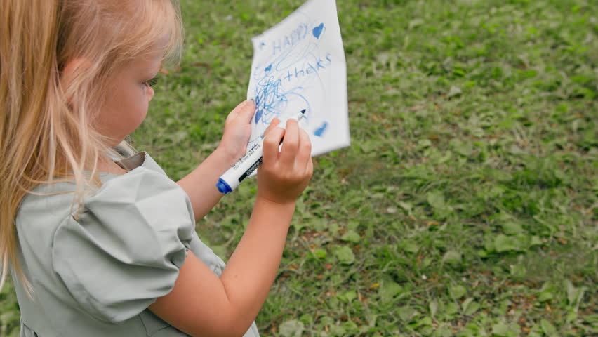portrait of an angry upset capricious girl in a dress in the park draws a postcard with felt-tip pen gets annoyed and sketches everything annoyingly