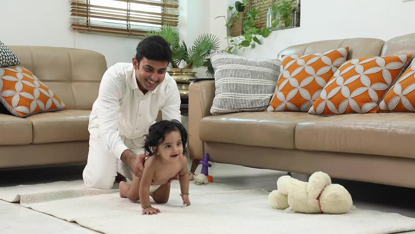 A happy father watches his infant crawl across the floor. 

