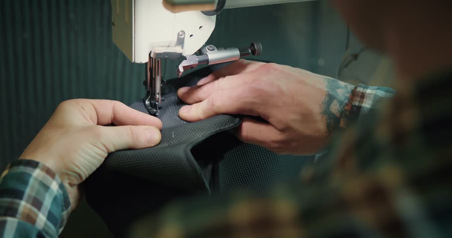 Male tailor works on sewing machine at the private workshop. Male seamstress is sewing fabrics for shoes in a shoe workshop. Shoe making process
