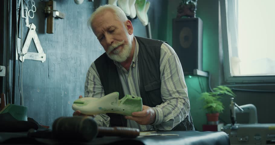 Mature shoemaker working on a shoe last at the workshop. Aged craftsman holding a shoe last in hands and thinking about new model. Shoes making process