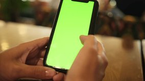 Close-up of female hands holding smartphone. Point of view of woman at phone with green screen. Chromakey lady watching video news close up, flipping through the news feed in social networks.