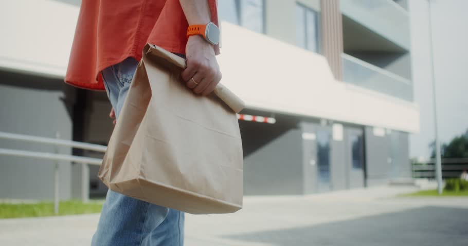 A man carries a paper bag with ready-made food walking around the city, close-up of his hands, no face