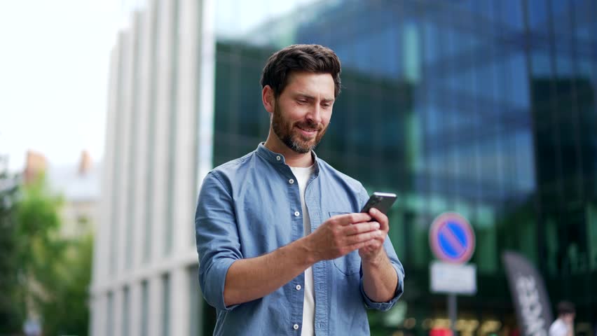 Handsome happy bearded businessman in casual walking near modern business office building hold smartphone in hands. Matureadult Man entrepreneur seo manager using read a mobile phone outside lifestyle Royalty-Free Stock Footage #1106282385