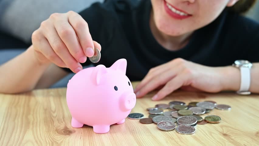 Happiness woman while putting a coin into piggy bank for saving money. A piggy bank is a small container used to save coins, often but not always shaped like a pig. Royalty-Free Stock Footage #1106282555