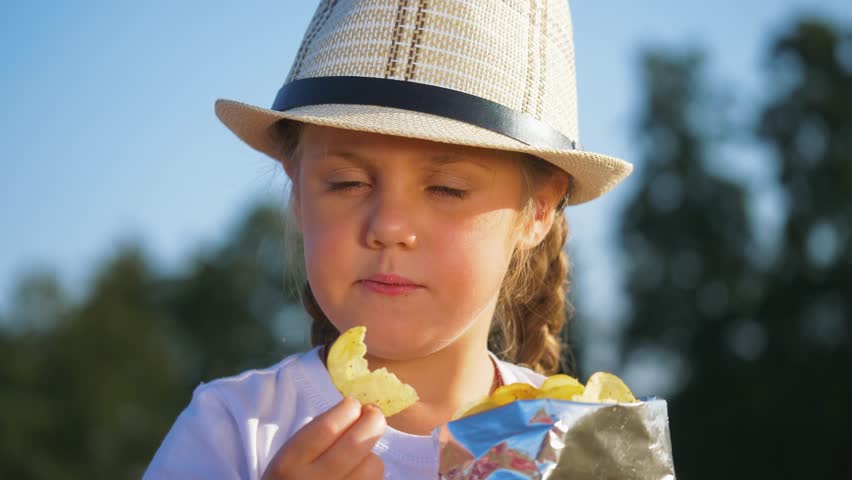 Happy little kid eat potato snack. Child eat unhealthy food. Child eats potato chips. Quick snack in nature in park with potato chips. Child eats chips from package