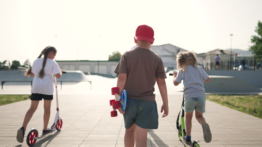 Happy cheerful children amusement park.Children in park engaged in active sports, riding skateboard, rollerblading, scooter. Children spent fun day park playing sports. Happy active childhood in park.