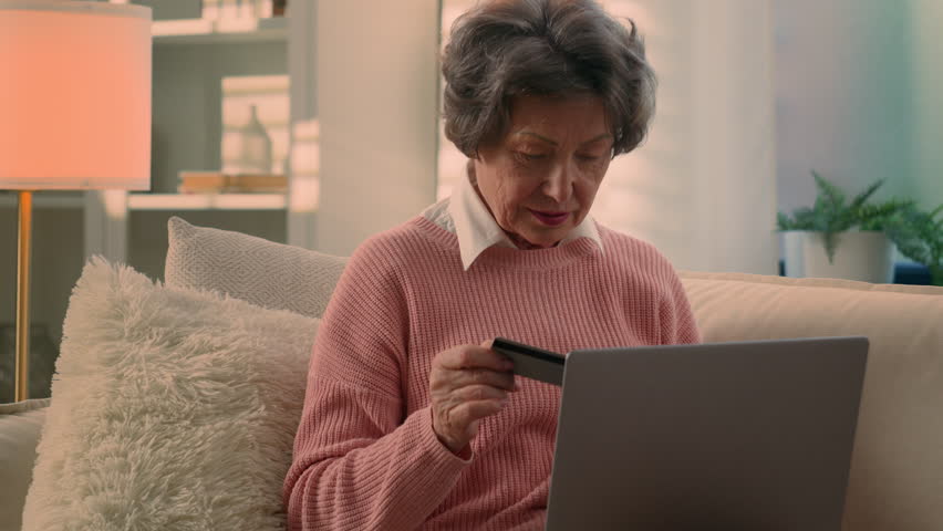 Happy Caucasian old woman senior granny elderly female mature lady retired grandmother with laptop and bank credit card paying online shopping with computer buying internet payment celebrate at home Royalty-Free Stock Footage #1106285547