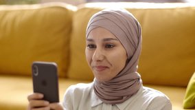 Funny online content. Close up portrait of young carefree muslim woman in hijab playing video games on smartphone, enjoying her positive results, slow motion, free space