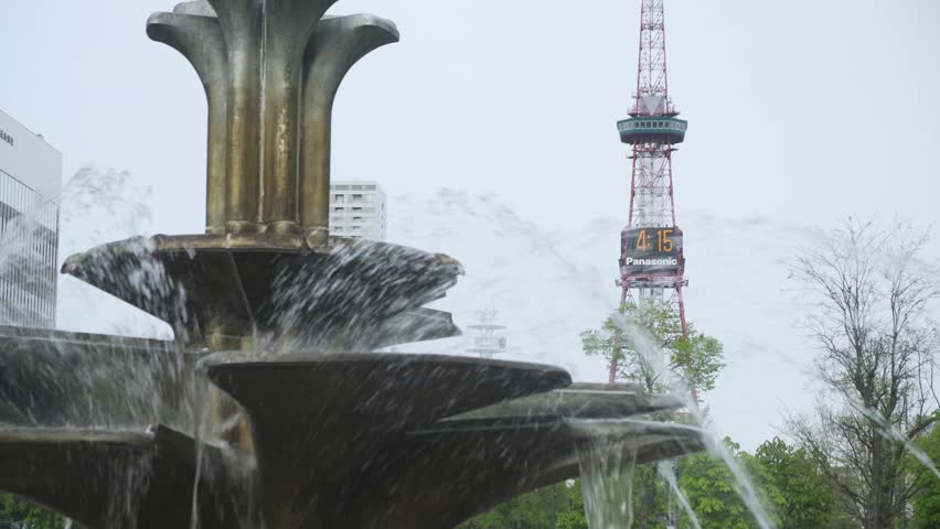 Blowing Water On The Fountain At Odori Park With Sapporo TV Tower At Background In Hokkaido, Japan. selective focus