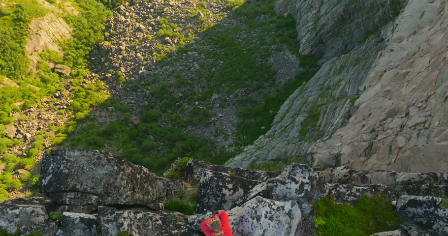 Drone reveal female mountain cliff edge drop looking at view in midnight sun