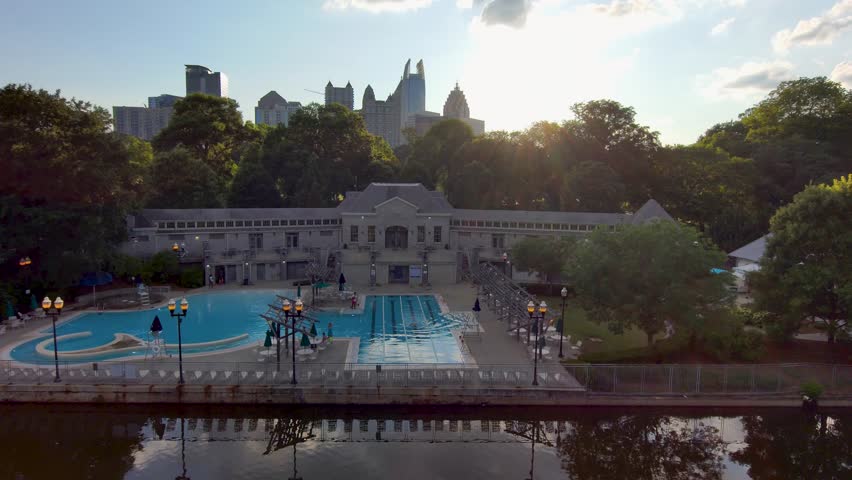 sideways aerial footage of a gorgeous summer landscape at Piedmont Park with the rippling waters of Lake Clara Meer, lush green trees and grass, a pool with people in Atlanta Georgia USA