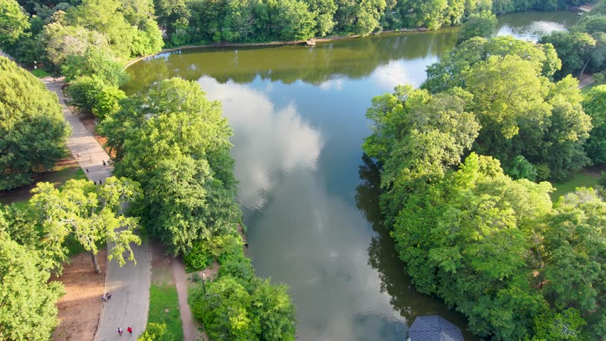 panning aerial footage of a gorgeous summer landscape at Piedmont Park with the rippling waters of Lake Clara Meer, lush green trees and grass, a pool and people walking in Atlanta Georgia USA
