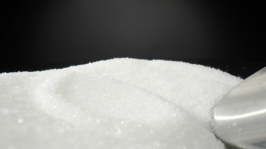 A macro video captures the delicate act of scooping pure white sugar with a spoon. The intricate crystals glisten and cascade, forming a sweet symphony of texture and light. Sugar background
