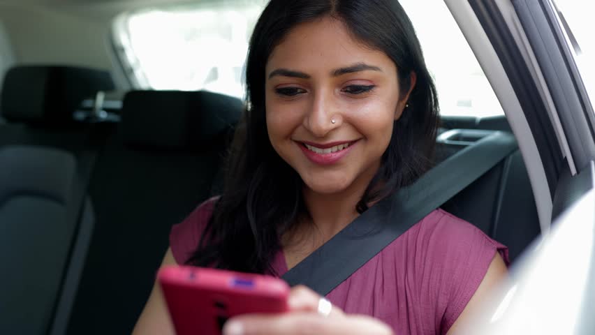 Happy young indian woman using cell phone sitting in the back seat of a car. Technology and transport concept. Royalty-Free Stock Footage #1106309287