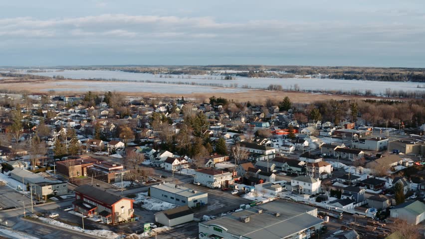 Slow aerial dolly left shot of snow covered town of Thurso Quebec Canada with the frozen Ottawa River visible in background on a winter day.