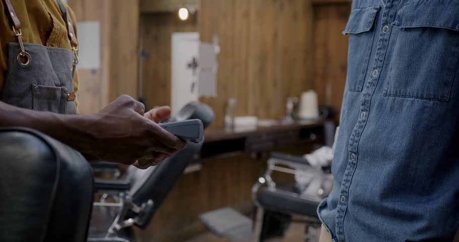 Close-up of male client paying for barbershop service with smart watch and terminal and shaking hands with barber. Wireless technology and NFC payment concept. Royalty-Free Stock Footage #1106313823