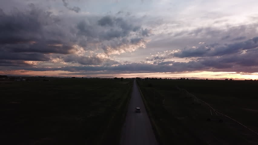 Aerial Tilt Down Shot Of Car On Road Amidst Plants At Dusk, Drone Flying Forward Over Landscape Against Cloudy Sky - Billings, Montana