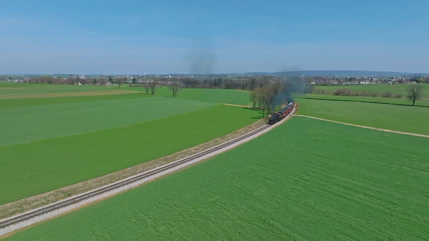Ronks, Pennsylvania, April 3, 2023 - An Aerial View of a Steam Passenger Train Traveling Blowing Smoke, on a Single Track, Coming Around a Curve on a Sunny Spring Day