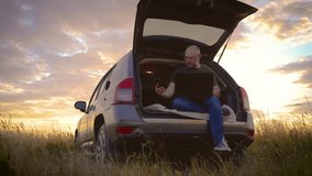 Caucasian bald business man freelancer working remotely with laptop and smartphone sitting in car trunk while traveling, general plan in field at sunset. Busy worker freelancer entrepreneur notebook - Powered by Shutterstock - Get 15% off with code: PIKWIZARD15