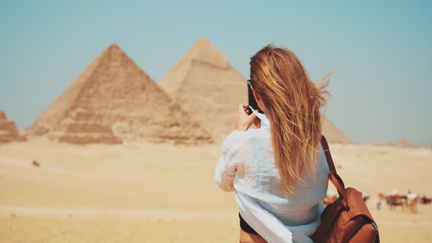 Tourist woman in takes photo on smartphone of Great Giza pyramids in Cairo Egypt enjoys attraction of world UNESCO ancient heritage, back view. Tourism travel wanderlust journey sightseeing concept. | Shutterstock HD Video #1106329143