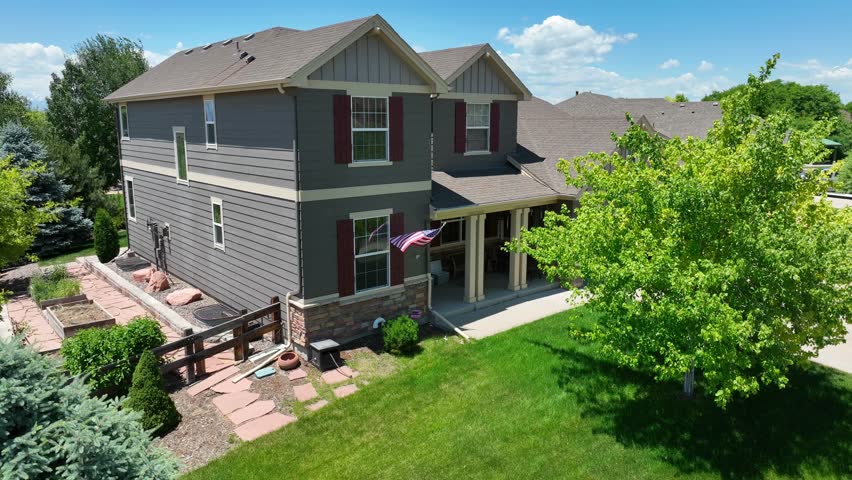 American flag waving on beautiful family house in Colorado. Aerial rising shot reveals sprawling neighborhood in summer with Rocky Mountains in distance.