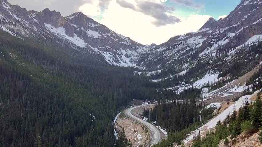 View of Highway 20 or the Cascade Loop road winding up stunning Washington Pass. Snow covered mountains surround the road - North Cascades National Park, Washington, USA