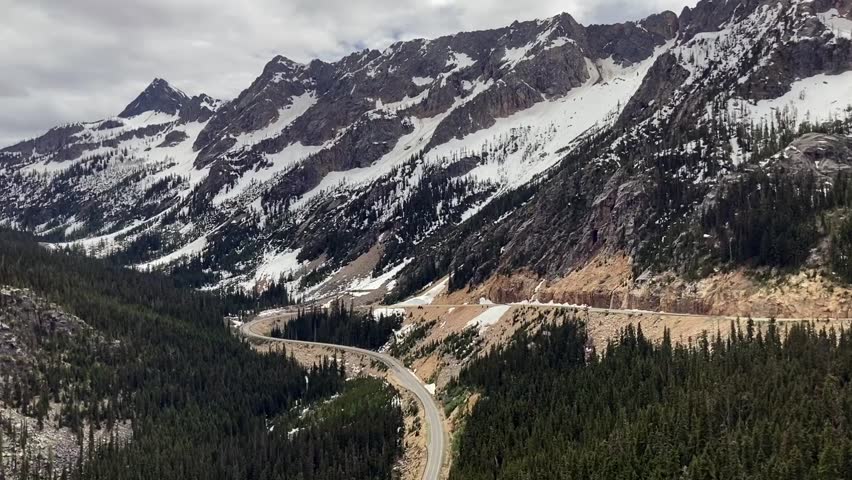 View of the Sharp curve switchback of Washington Pass road with beautiful snow covered mountains in the background. Highway 20 or the Cascade Loop - North Cascades National Park, Washington, USA