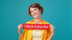 Positive young woman shows red sign with words Like and Subscribe. Smiling blogger shakes inscription attracting attention of users in turquoise studio - Powered by Shutterstock - Get 15% off with code: PIKWIZARD15