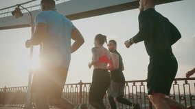 Young men and women in sportswear run in sunny summer morning. Athletes move along running track on footbridge across wide river slow motion low angle shot - Powered by Shutterstock - Get 15% off with code: PIKWIZARD15