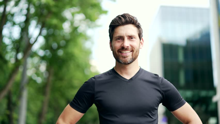 Portrait of happy bearded handsome sporty man in black t-shirt looking at camera. Mature adult sportsman runner on urban background outdoors outside healthy lifestyle morning workout on city street Royalty-Free Stock Footage #1106340549