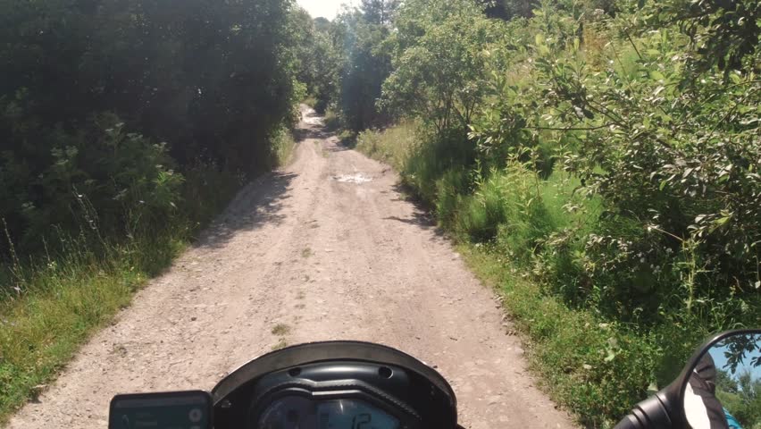 Motorcycle low speed riding on the dirt country road, adventure moto traveling in the summer, first person point of view, pov