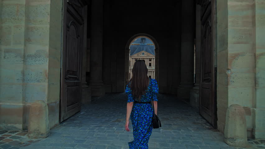 A young woman visiting and walking to The Court of Honor of Hotel National des Invalides in Paris. A tourist looking at the Golden Dome of the Hotel des Invalides and the rooftops of Paris.
