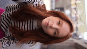 Vertical POV portrait of attractive redhead female taking selfie on smartphone camera sitting at table in outdoor cafe. Point of view of pretty young woman doing selfie photo on mobile phone camera